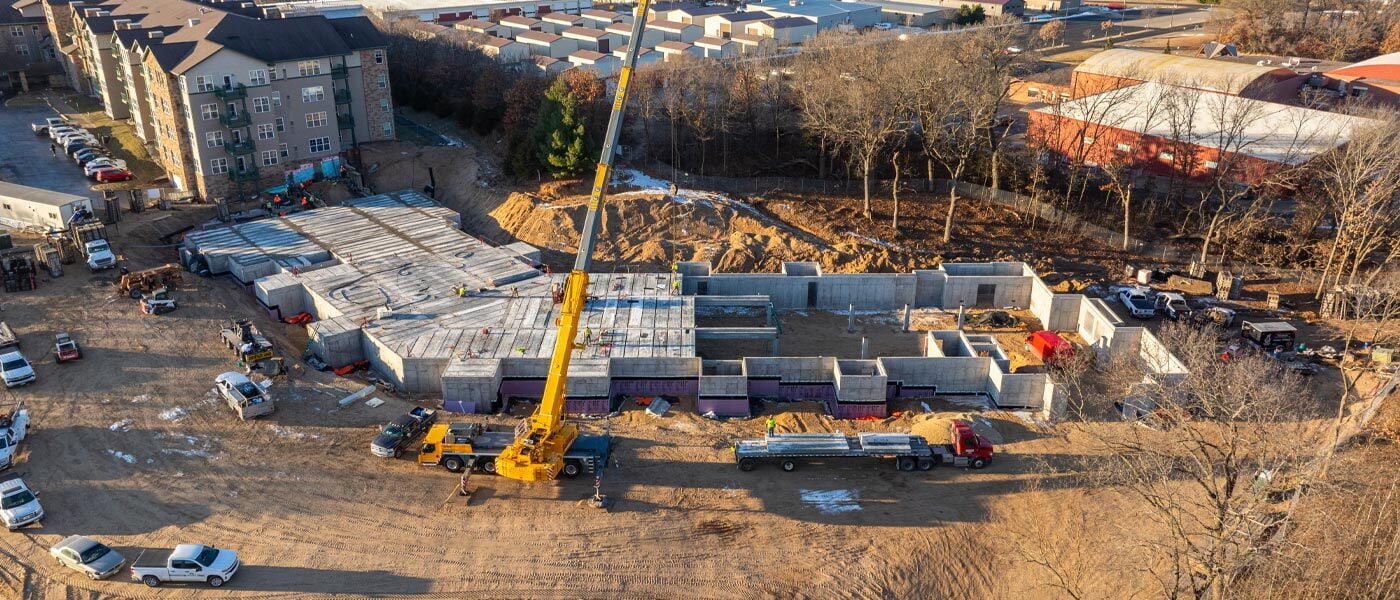 Overhead view of a yellow crane towering over the construction site of an apartment complex, with hollowcore plank covering half of the new building’s podium.